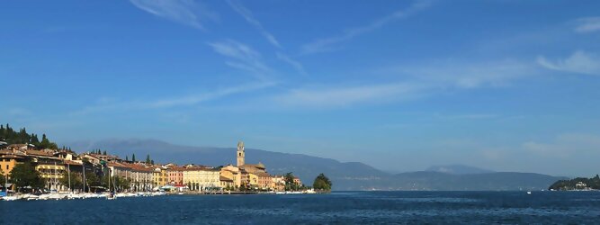 Trip Coupons beliebte Urlaubsziele am Gardasee -  Mit einer Fläche von 370 km² ist der Gardasee der größte See Italiens. Es liegt am Fuße der Alpen und erstreckt sich über drei Staaten: Lombardei, Venetien und Trentino. Die maximale Tiefe des Sees beträgt 346 m, er hat eine längliche Form und sein nördliches Ende ist sehr schmal. Dort ist der See von den Bergen der Gruppo di Baldo umgeben. Du trittst aus deinem gemütlichen Hotelzimmer und es begrüßt dich die warme italienische Sonne. Du blickst auf den atemberaubenden Gardasee, der in zahlreichen Blautönen schimmert - von tiefem Dunkelblau bis zu funkelndem Türkis. Majestätische Berge umgeben dich, während die Brise sanft deine Haut streichelt und der Duft von blühenden Zitronenbäumen deine Nase kitzelt. Du schlenderst die malerischen, engen Gassen entlang, vorbei an farbenfrohen, blumengeschmückten Häusern. Vereinzelt unterbricht das fröhliche Lachen der Einheimischen die friedvolle Stille. Du fühlst dich wie in einem Traum, der nicht enden will. Jeder Schritt führt dich zu neuen Entdeckungen und Abenteuern. Du probierst die köstliche italienische Küche mit ihren frischen Zutaten und verführerischen Aromen. Die Sonne geht langsam unter und taucht den Himmel in ein leuchtendes Orange-rot - ein spektakulärer Anblick.